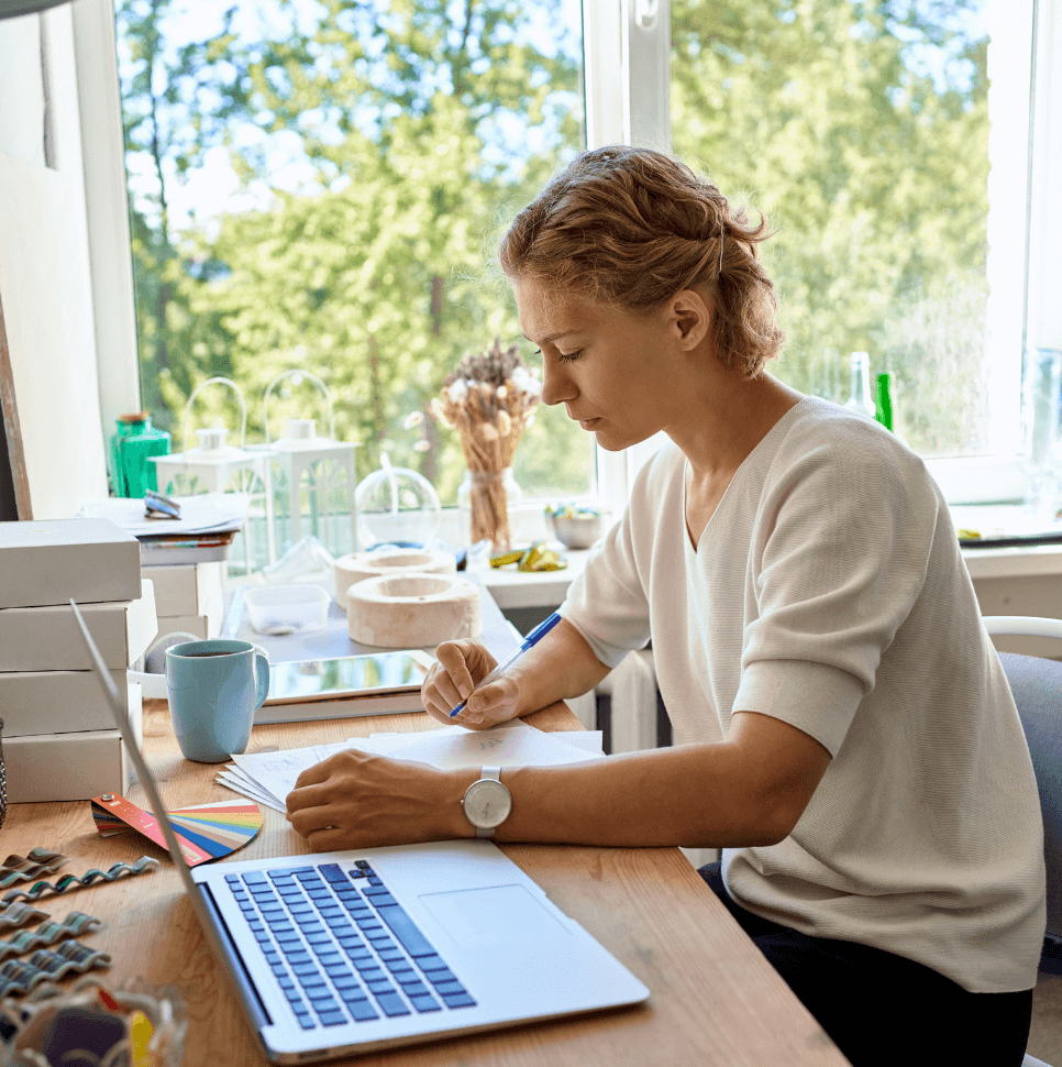 Femme qui écrit sur papier à côté d'un ordinateur