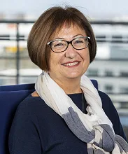 Sylvie Husson souriante est photographiée assise sur un fauteuil bleu, avec un foulard blanc et gris